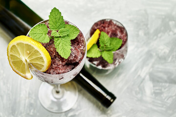 frozen red wine in two glass glasses decorated with a slice of lemon and lemon leaves and an empty glass bottle