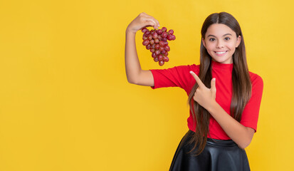 happy teen kid hold bunch of grapes on yellow background