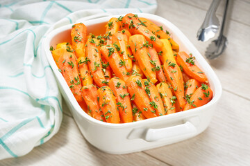 Roasted baby carrots with fresh thyme in a ceramic form on a light background.
