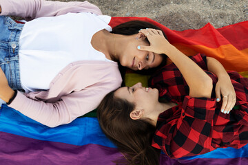A beautiful lesbian young couple embraces and holds a rainbow flag. Girls enjoy at the beach.