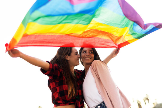 A beautiful lesbian young couple embraces and holds a rainbow flag. Girls enjoy at the beach.