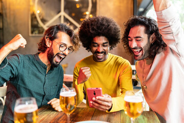 Three excited multiracial friends celebrating victory and winning online bet on match using betting online sport app on mobile phone