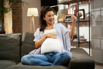 Obraz premium Pregnant woman with ultrasound photo. Beautiful pregnant woman enjoy at home.