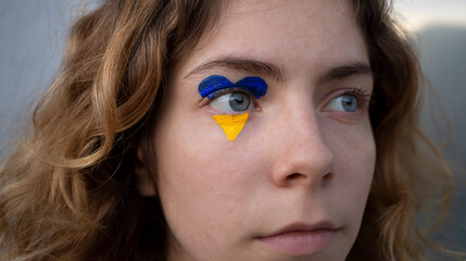 close-up of female face with painted yellow - blue heart around eye. Stop Russian aggression in Ukraine. Hope and faith, fear, helplessness. appeal to world community for help to the Ukrainians