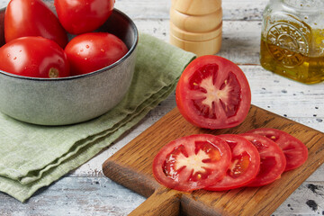 Fresh raw tomatoes on a cutting board on a white wooden table, close-up