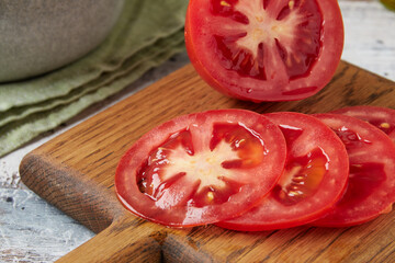 Fresh raw tomatoes on a cutting board on a white wooden table, close-up