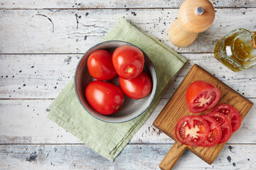 Fresh tomatoes in a plate on a white wooden background, top view