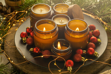 Soy candles burn in glass jars. Comfort at home. Candle in a brown jar. Scent and light. Scented handmade candle. Aroma therapy. Christmas tree and winter mood. Cozy decor. Festive garland decoration
