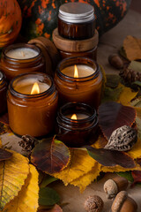 Soy candles burn in glass jars. Tree leaves. Comfort at home. Candle in a brown jar. Scent and light. Scented handmade candle. Aroma therapy. Autumn mood. Cozy home decor in fall. Festive decoration.