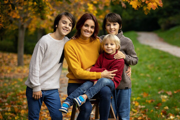 Fototapeta premium Cute blond toddler child and sibling brothers, standing next to autumn wooden stand with decoration, apples, leaves, mug, hedgehock in the park