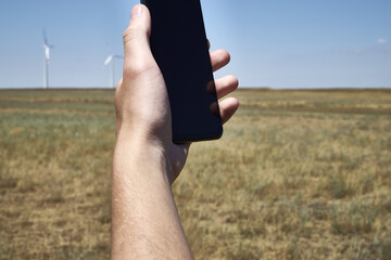 a man holds a smartphone in his hand against the background of a modern wind farm . Mobile phone communication. Modern communication.
