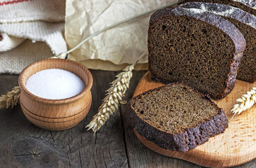 Close-up view of salt with traditional sliced bread and spikelets of wheat on wooden background