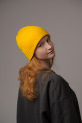 young girl model in yellow cap and gray coat isolated on gray background. Product photo mockup for fashion brands and marketplaces, woolen cap, turkish textiles.