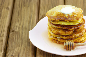Stack of pancakes with honey and piece of butter on wooden table