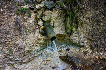 A descending spring flowing from a pipe in the forest