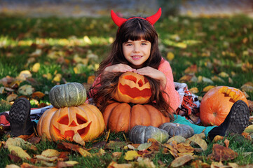 Pretty girl  at the autumn lawn with carved Halloween pumpkins