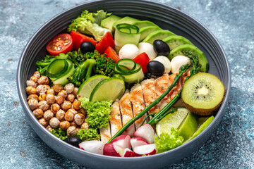 Grilled chicken, avocado, asparagus, chickpeas, broccoli, radish, cucumber, tomatoes, olives, mozzarella buddha bowl on dark background, top view. Delicious balanced food concept