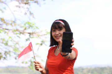 young asian woman is on the phone and holding the indonesian flag with a happy face
