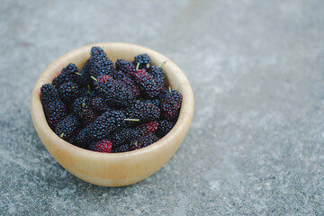 Black mulberry in wooden cup on cement floor It is a healthy berry with a sweet and sour taste.
