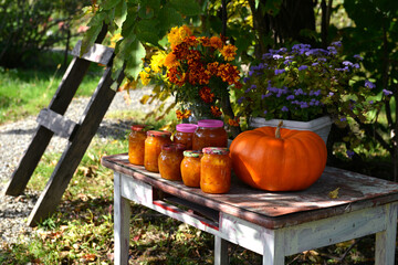 Vintage still life with jars of pumkin jam and fall flowers on the old table in the garden outside