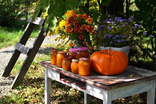 Vintage still life with jars of pumkin jam and fall flowers on the old table in the garden outside