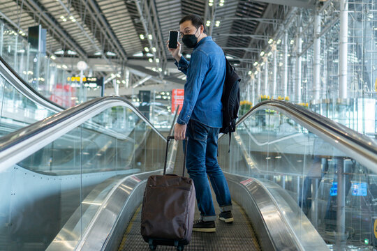 Young middle man travel by airplane with suitcase at airport terminal to flight gate. Asian guy with bagpack walking on travelator at airport. Traveler with luggage on moving walkway.Travel concept.