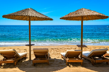 Two sun umbrellas and four sunbeds ready for tourists on sandy beach