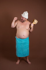 A fat man in a blue towel and a bath hat. Rest in the sauna. Happy guy on a brown background.