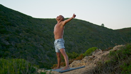Sportsman training yoga mat at green mountain view. Focused man stretching alone