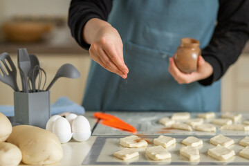 Obraz na płótnie Canvas A chef in a blue apron sprinkles cinnamon on cookie dough blanks in a home private bakery.