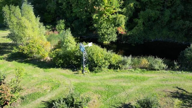 Orbital aerial view of windmill at the edge of river and orchard