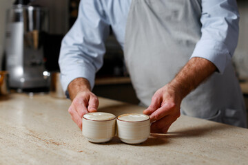 Barista pouring two cups of cappuccino in coffee shop
