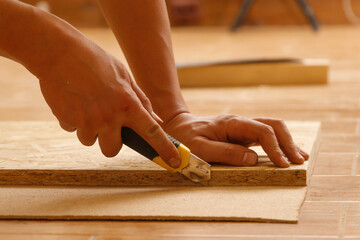Side view of the hands of a Carpenter who cuts fiberboard while making furniture to order.