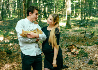 Young pregnant woman, her husband and their red cat in park. Happy family outdoors. Expecting for firstborn