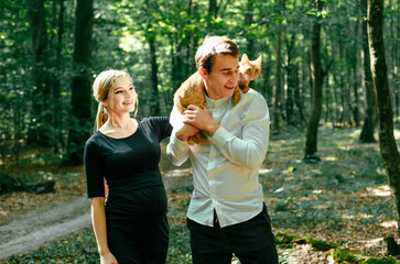 Young pregnant woman, her husband and their red cat in park. Happy family outdoors. Expecting for firstborn