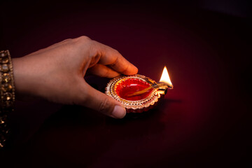Happy Diwali. Woman hands holding lit candle isolated on red  background. Diwali celebration