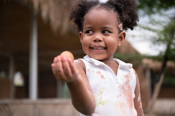 Happy African American kid girl holding egg chicken at farm