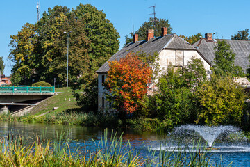 Fototapeta na wymiar autumn landscape with historic mill building by the river and fountain, Dobele, Latvia