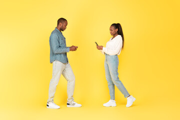 Black Man And Woman Using Smartphones Texting Over Yellow Background