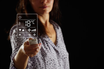 A woman in pajamas sets the temperature in the heating and air conditioning system of a bedroom,...