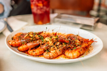 Traditional Spanish tapas. Aromatic delicious grilled king prawns with herbs and garlic pepper sauce on a white plate in a restaurant. Spanish cuisine dish. 