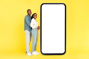 Fototapeta na wymiar Loving African American Couple Embracing Near Large Smartphone, Yellow Background