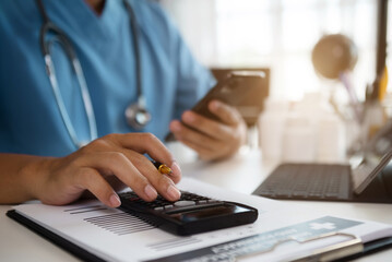Doctor hold smartphone, conduct financial transactions with calculate expenses - income and data documents, put on the desk