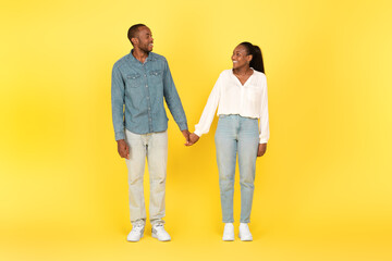 Cheerful Black Millennial Couple Holding Hands Posing On Yellow Background