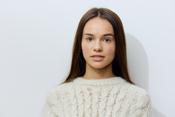 attractive, young woman stands in a white stylish sweater on a light background pleasantly looking at the camera with well-groomed hair