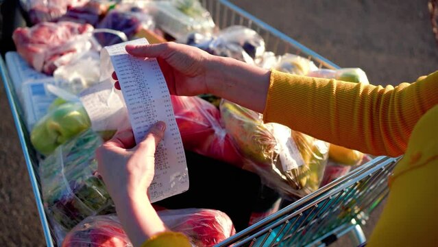 Worried woman checks a paper receipt after grocery shopping at a supermarket. Covid-19 global economy financial crisis concept, money saving. Food and grocery shopping