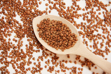 small grains of brown natural buckwheat in a wooden spoon