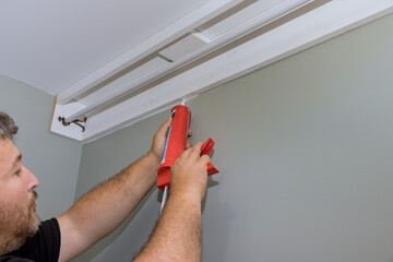 Seam between cornice and wall is filled with acrylic latex caulk silicone sealant by construction worker using syringe © ungvar
