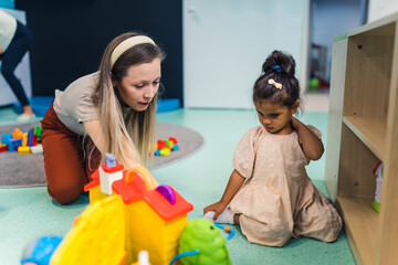 lovely little girl and her teacher having fun at the nursery, toys in the background. High quality photo
