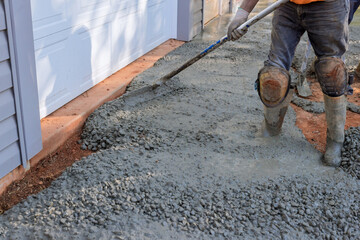 Construction contractors pouring wet concrete while paving driveway as they work on concrete...